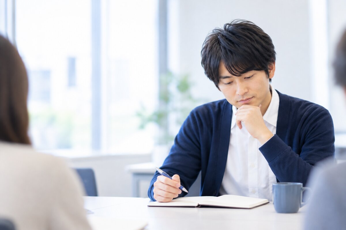 会議の最中に、うつむいてノートを見ながら言葉を探している会社員